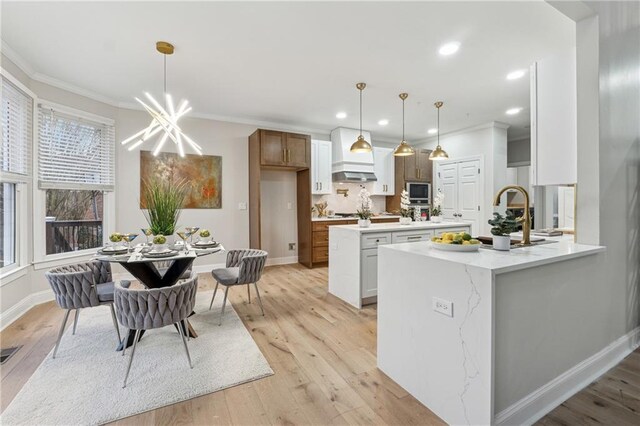 kitchen featuring ornamental molding, white cabinets, decorative light fixtures, and light wood finished floors