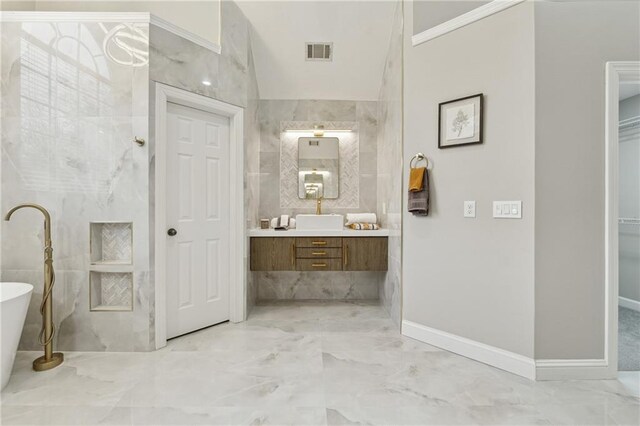 bathroom featuring vanity, visible vents, a freestanding bath, marble finish floor, and tile walls