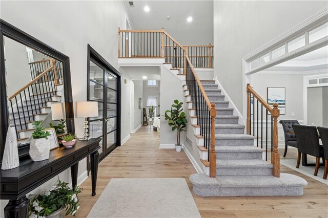 foyer entrance with light wood-style flooring, a high ceiling, baseboards, and stairs