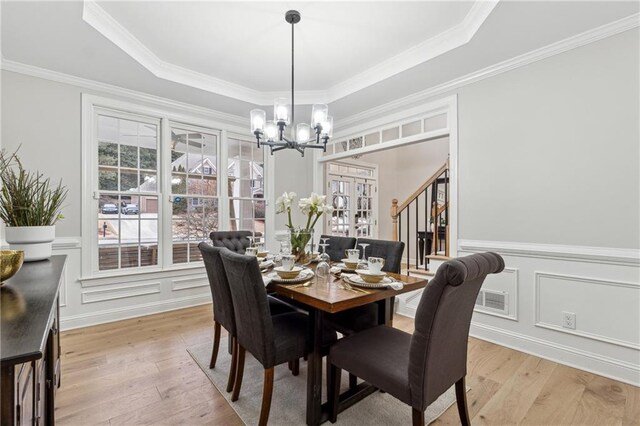 dining area featuring a tray ceiling, light wood finished floors, an inviting chandelier, and a decorative wall