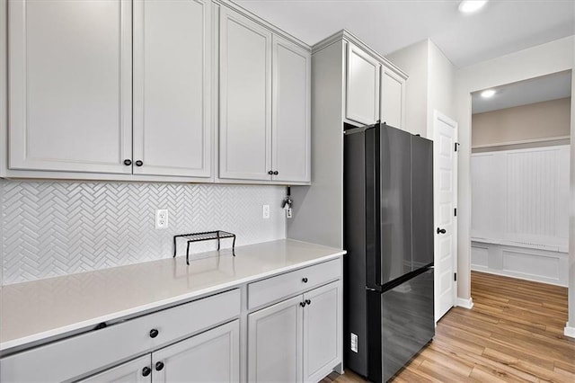 kitchen featuring light hardwood / wood-style floors, backsplash, and black refrigerator