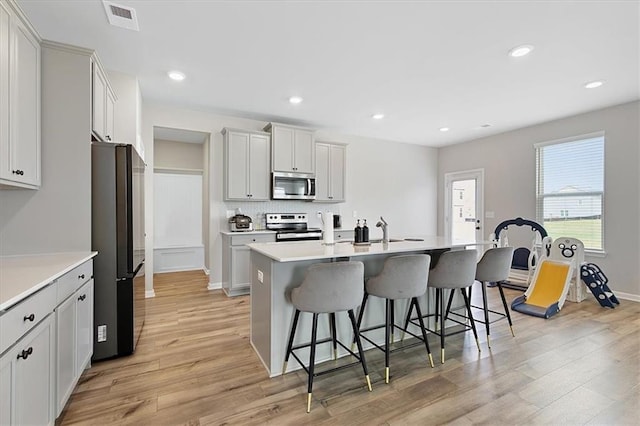 kitchen featuring white cabinetry, appliances with stainless steel finishes, light wood-type flooring, and an island with sink