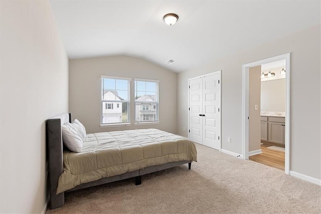 bedroom with connected bathroom, light carpet, a closet, and vaulted ceiling