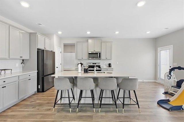 kitchen with appliances with stainless steel finishes, sink, an island with sink, light hardwood / wood-style floors, and a breakfast bar