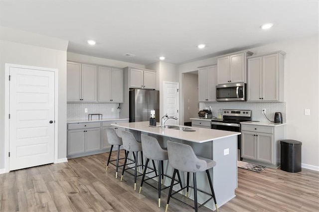 kitchen with appliances with stainless steel finishes, light hardwood / wood-style flooring, a center island with sink, and a kitchen breakfast bar