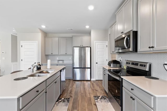 kitchen with a kitchen island with sink, sink, appliances with stainless steel finishes, and wood-type flooring