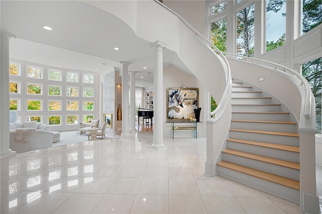 foyer entrance with a towering ceiling, a healthy amount of sunlight, light tile patterned floors, and decorative columns