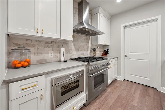 kitchen featuring white cabinetry, light hardwood / wood-style flooring, stainless steel range, decorative backsplash, and wall chimney range hood