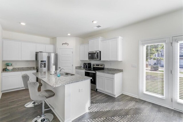 kitchen featuring appliances with stainless steel finishes, white cabinets, a center island with sink, and sink