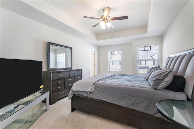 bedroom featuring a raised ceiling, light colored carpet, and ceiling fan