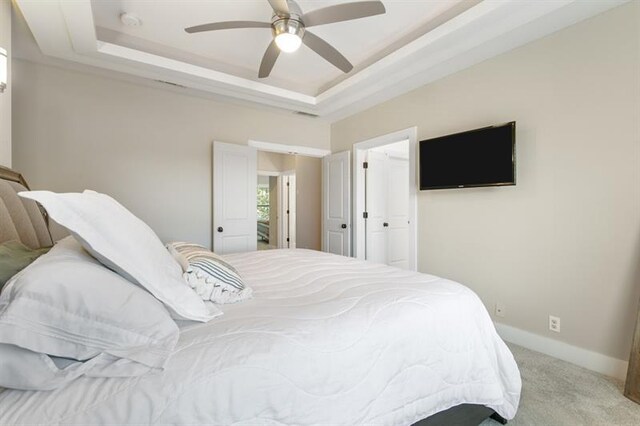 carpeted bedroom with ceiling fan and a tray ceiling