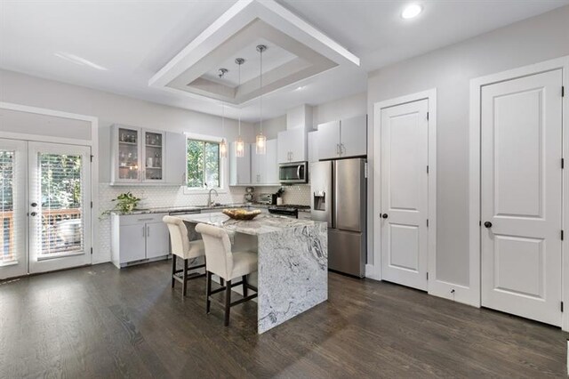 kitchen featuring appliances with stainless steel finishes, pendant lighting, white cabinets, a center island, and a raised ceiling