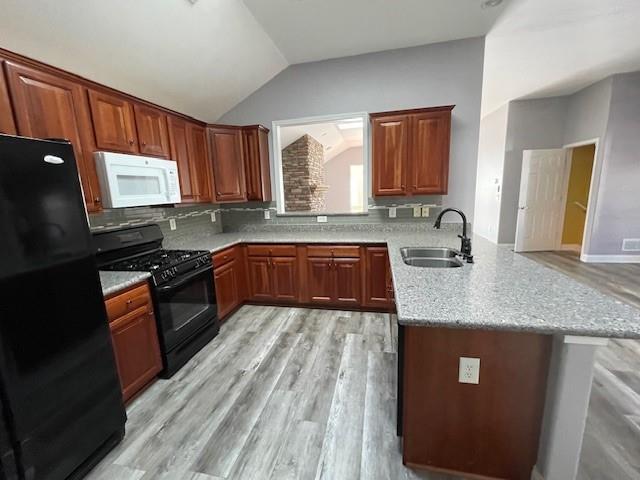 kitchen featuring kitchen peninsula, light stone countertops, black appliances, backsplash, and sink