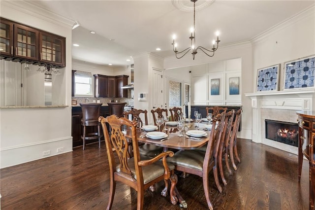 dining space featuring a tiled fireplace, ornamental molding, dark wood-style floors, and an inviting chandelier
