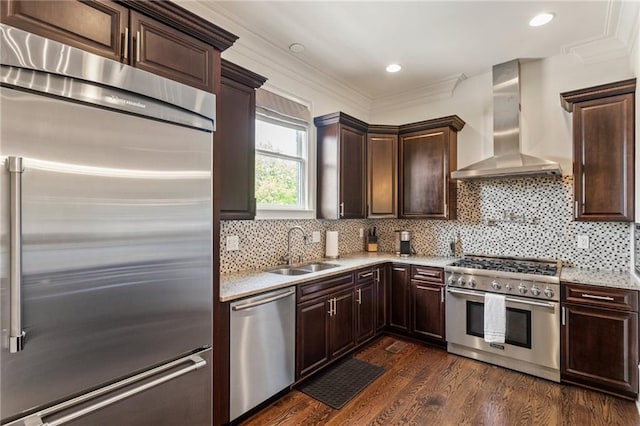 kitchen featuring dark brown cabinetry, dark wood finished floors, a sink, premium appliances, and wall chimney exhaust hood