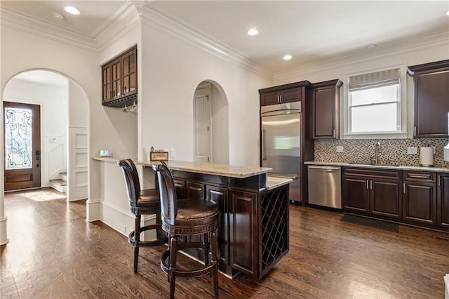 kitchen with a sink, arched walkways, stainless steel appliances, and dark wood-style floors