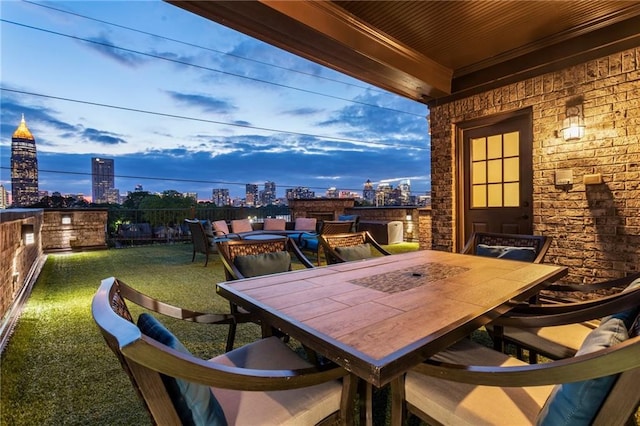 patio terrace at dusk featuring a yard, a city view, outdoor dining area, and a fenced backyard