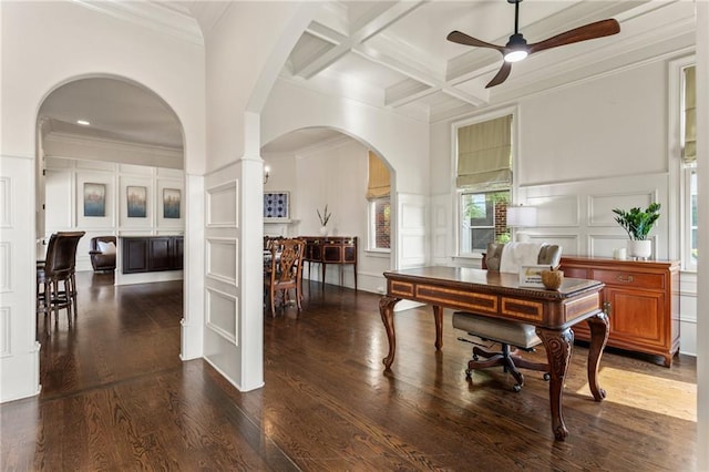 office area with wood finished floors, a decorative wall, beamed ceiling, ceiling fan, and arched walkways