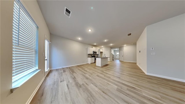 unfurnished living room featuring light wood-style floors, visible vents, and baseboards