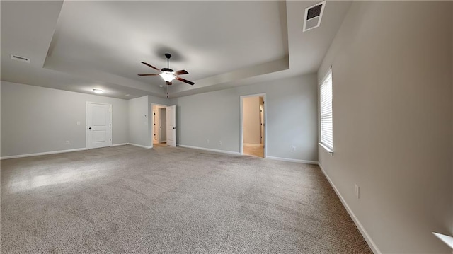 carpeted empty room with a tray ceiling, visible vents, and baseboards