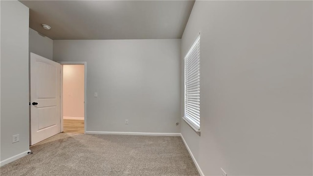 spare room featuring light carpet and baseboards