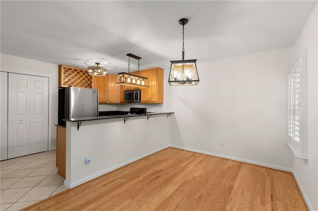 kitchen featuring pendant lighting, light hardwood / wood-style flooring, stainless steel refrigerator, a breakfast bar, and kitchen peninsula