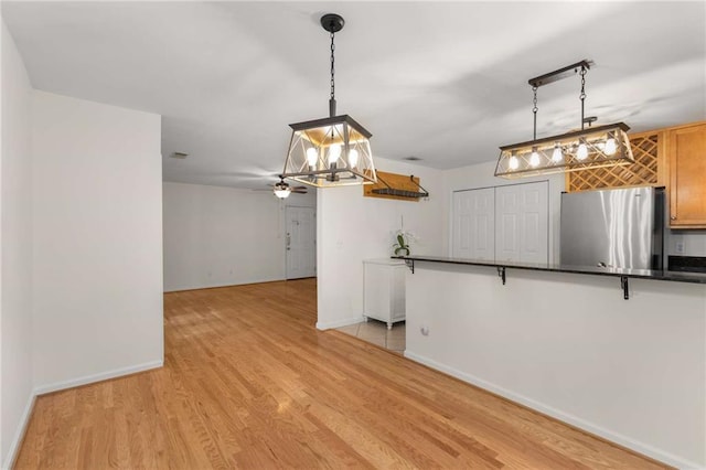 kitchen featuring stainless steel fridge, a kitchen bar, hanging light fixtures, light hardwood / wood-style floors, and kitchen peninsula