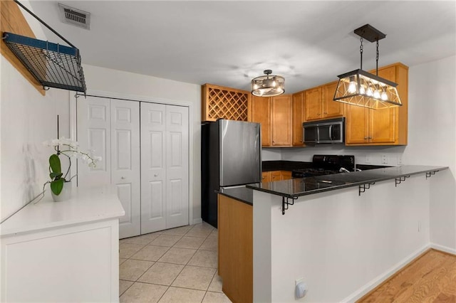 kitchen featuring a breakfast bar, stainless steel appliances, decorative light fixtures, and kitchen peninsula