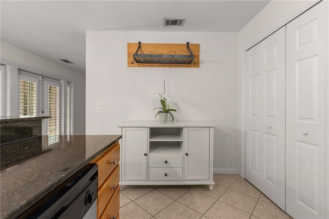 interior space with white cabinetry, stainless steel dishwasher, dark stone counters, and light tile patterned flooring