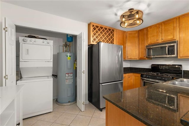 kitchen featuring light tile patterned flooring, dark stone countertops, stacked washer and dryer, stainless steel appliances, and electric water heater