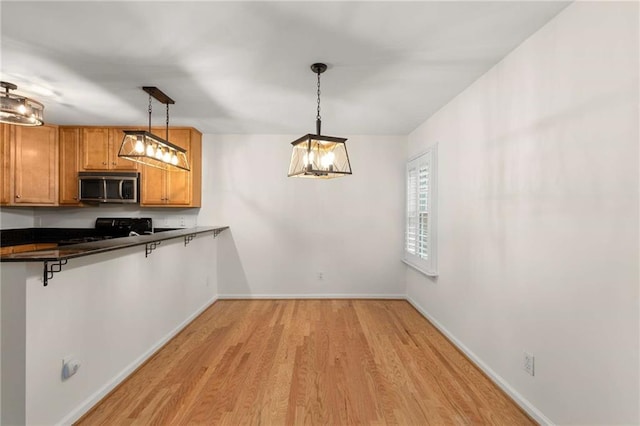 kitchen with a breakfast bar, kitchen peninsula, pendant lighting, light hardwood / wood-style floors, and stove