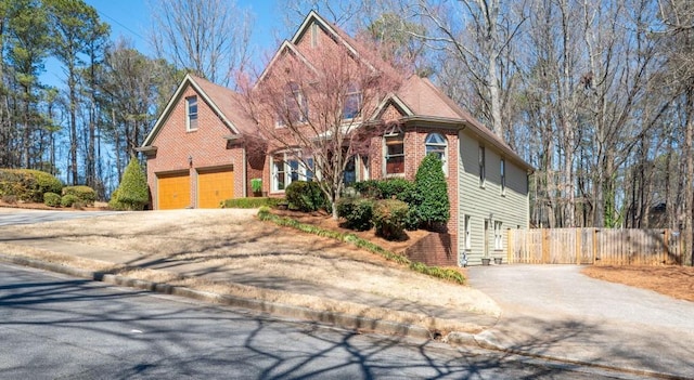 view of front of home featuring a garage, fence, brick siding, and driveway