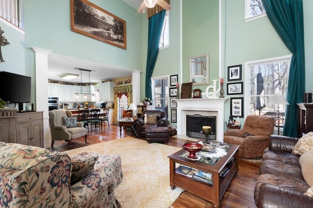 living room with decorative columns, a high ceiling, wood finished floors, and a fireplace