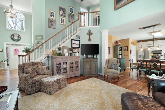 living room featuring wood finished floors, stairway, a high ceiling, an inviting chandelier, and ornate columns