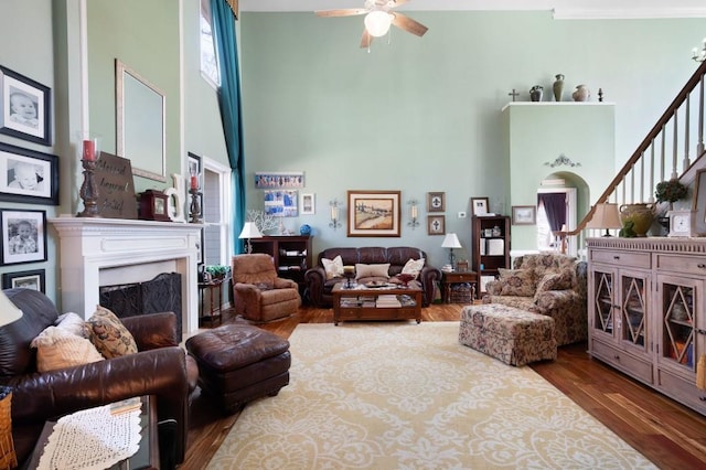 living area featuring ceiling fan, stairway, a premium fireplace, a towering ceiling, and wood finished floors