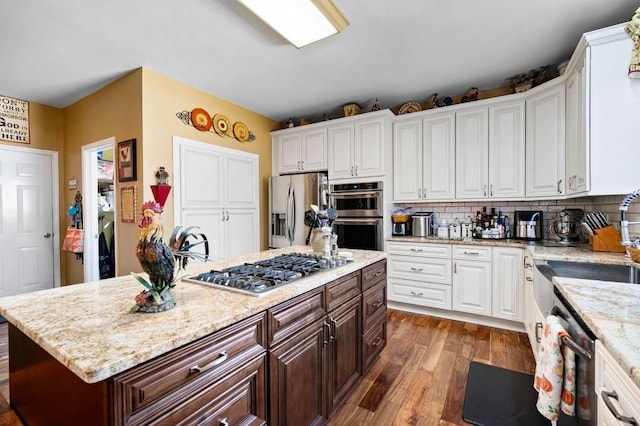 kitchen with dark wood finished floors, a sink, stainless steel appliances, white cabinetry, and tasteful backsplash