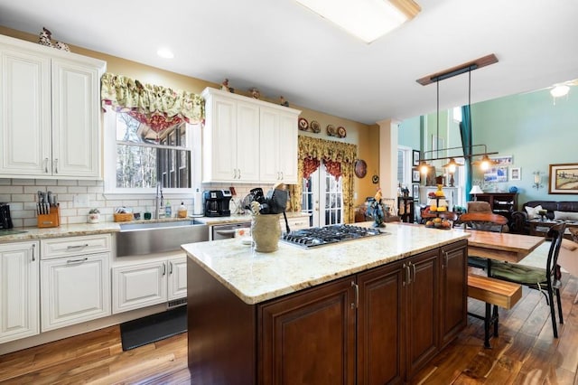 kitchen featuring wood finished floors, a sink, decorative backsplash, stainless steel gas stovetop, and a wealth of natural light