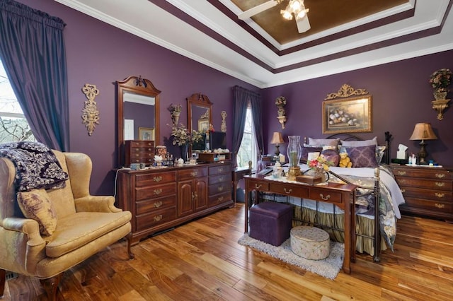 bedroom featuring a raised ceiling, a ceiling fan, wood finished floors, and crown molding