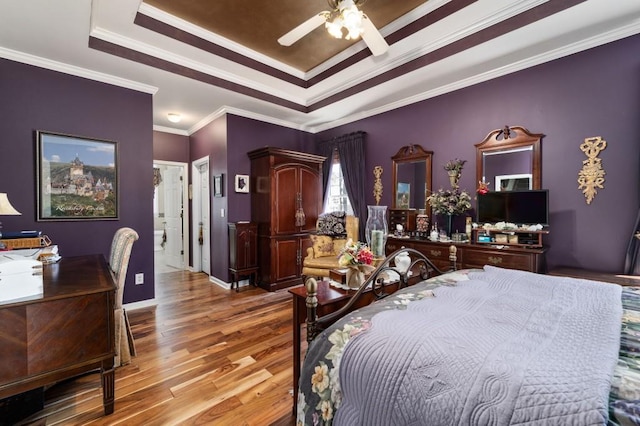 bedroom featuring a tray ceiling, wood finished floors, baseboards, and ornamental molding