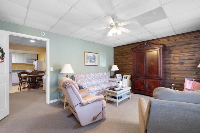 living room with a drop ceiling, baseboards, a ceiling fan, and carpet floors