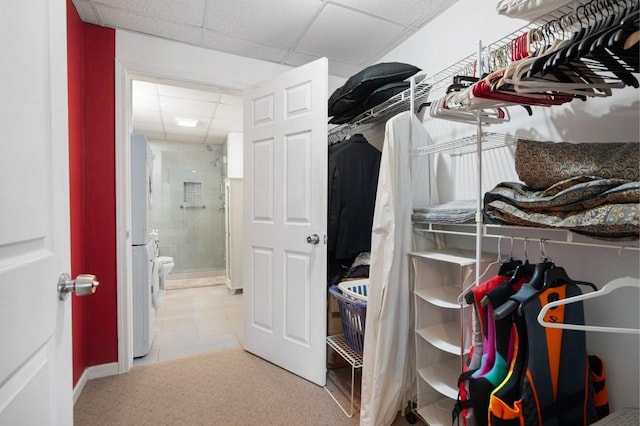 spacious closet with tile patterned flooring, stacked washer / dryer, a paneled ceiling, and carpet