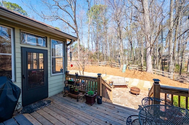 wooden terrace with outdoor dining area, a fire pit, a grill, and fence