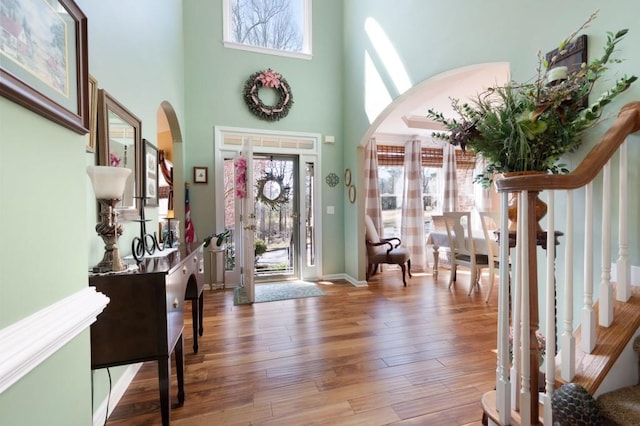 entryway with arched walkways, a high ceiling, wood finished floors, and stairs