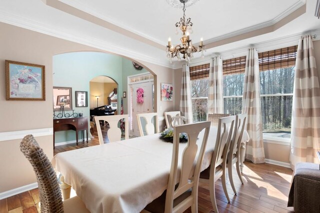 dining area featuring crown molding, baseboards, wood finished floors, arched walkways, and a raised ceiling