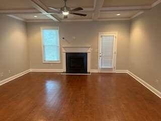 unfurnished living room featuring dark wood-type flooring, coffered ceiling, ornamental molding, beamed ceiling, and ceiling fan