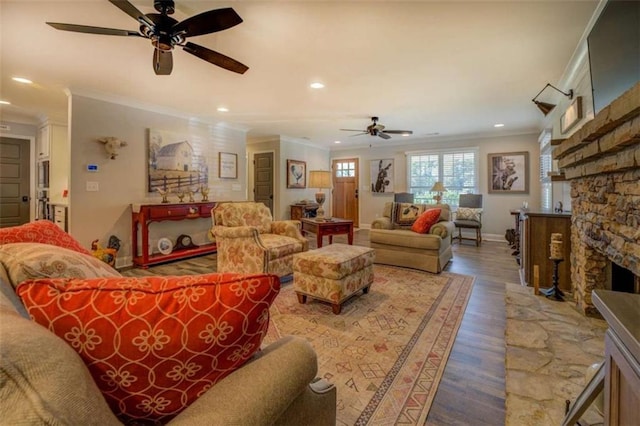 living room with hardwood / wood-style flooring, a stone fireplace, ceiling fan, and crown molding