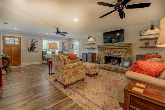 living room with ceiling fan, wood-type flooring, crown molding, and a stone fireplace