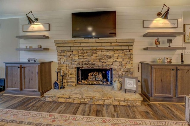 unfurnished living room featuring a stone fireplace, wood walls, and dark wood-type flooring