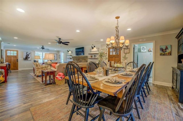 dining area featuring ceiling fan with notable chandelier, wood-type flooring, ornamental molding, and a fireplace