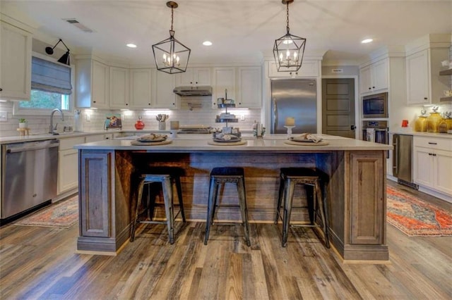 kitchen with hardwood / wood-style flooring, white cabinetry, built in appliances, and a kitchen island